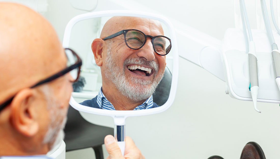 older man loving his new smile with dental implants at the dentist